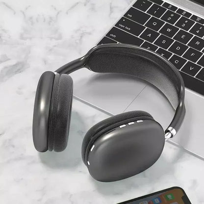 Black wireless over-ear headphones on marble surface beside laptop keyboard and smartphone