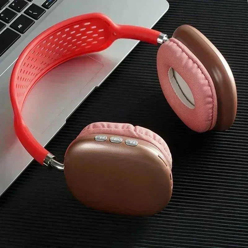 Red and brown wireless headphones with control buttons on earcup, placed next to a laptop on a black surface