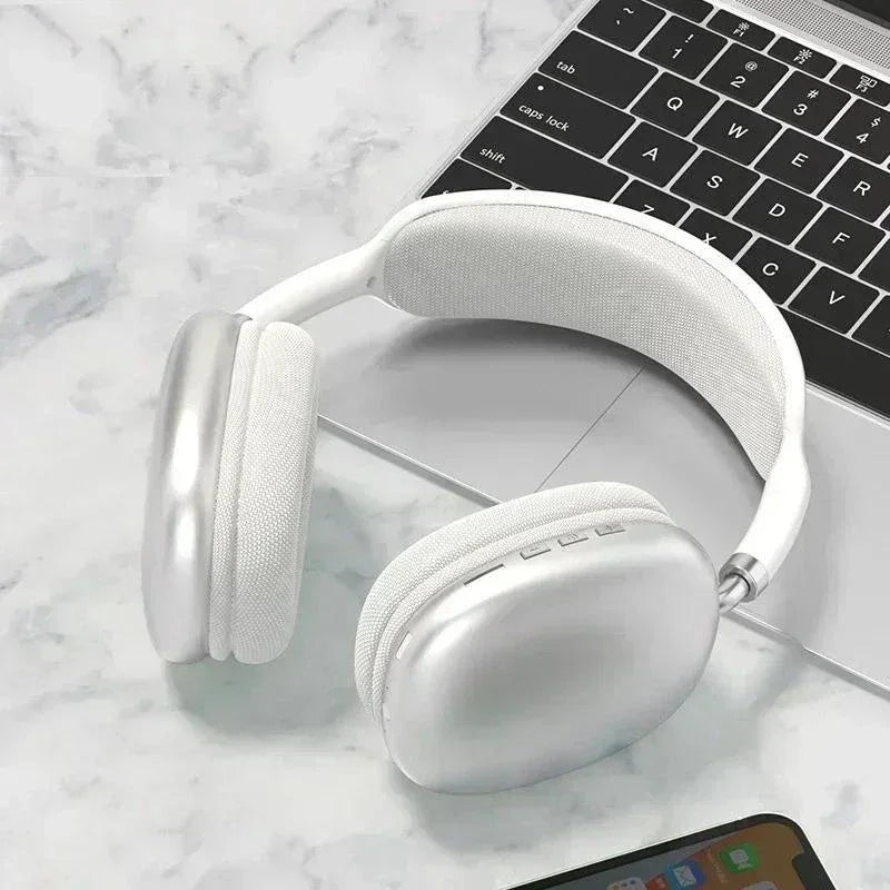 Silver wireless over-ear headphones on marble surface with partial laptop and smartphone