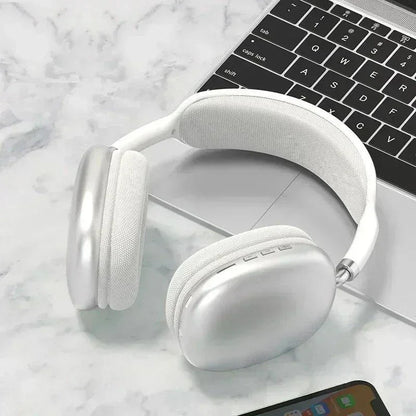 Silver wireless over-ear headphones on marble surface with partial laptop and smartphone